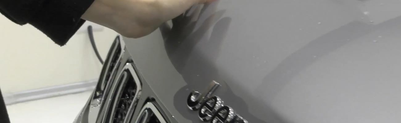 Detail of a professional auto detailer's hand applying a protective ceramic coating to the emblem of a car, ensuring precise and thorough coverage.